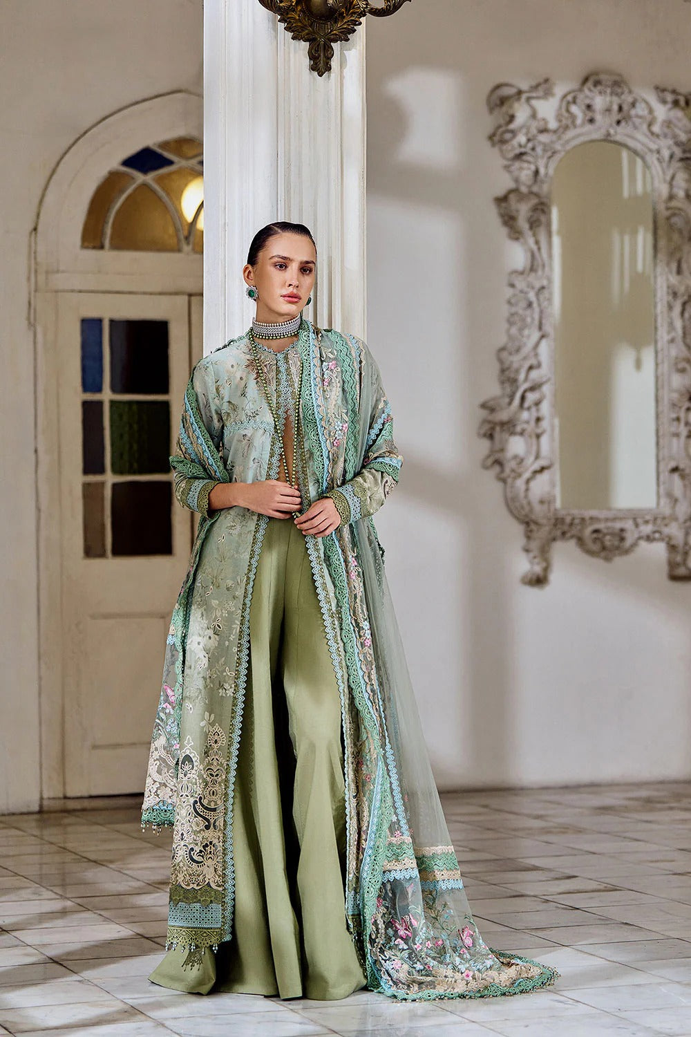 Woman in a green and patterned outfit standing in a room with a decorative mirror.