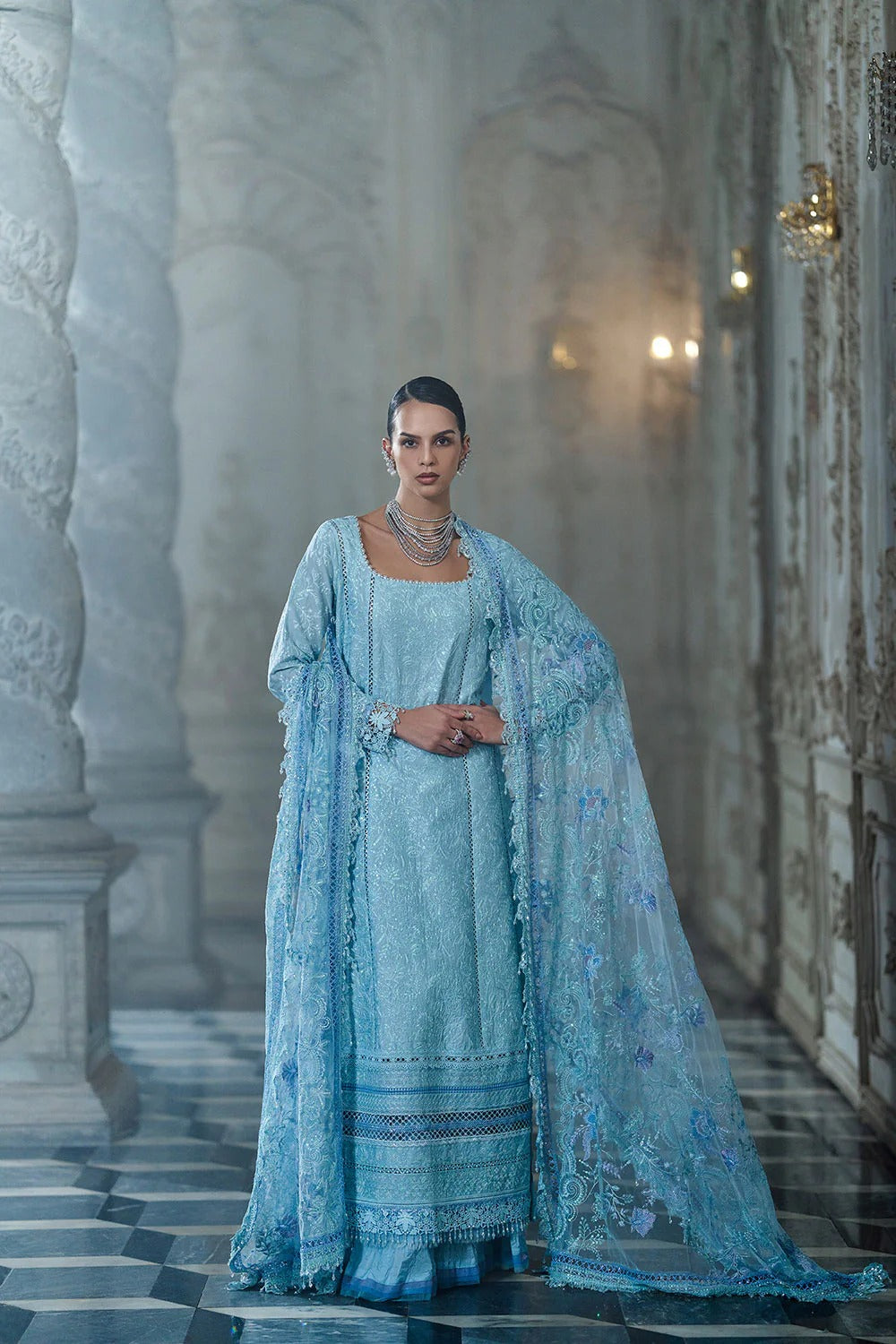 Woman in a light blue traditional outfit standing in an ornate hallway.