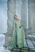 Woman in a light green embroidered dress standing in a classical architecture setting.