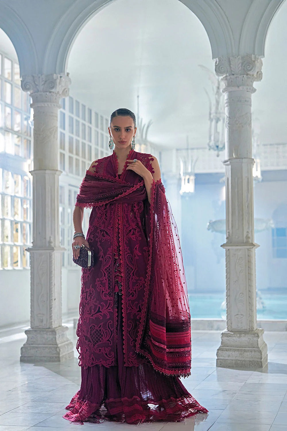 Woman in a vibrant pink traditional outfit standing in an elegant white architectural setting.
