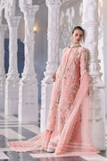 Woman in a pink embroidered outfit standing against white marble columns.