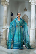Woman in a teal and blue traditional outfit standing in an elegant indoor setting.