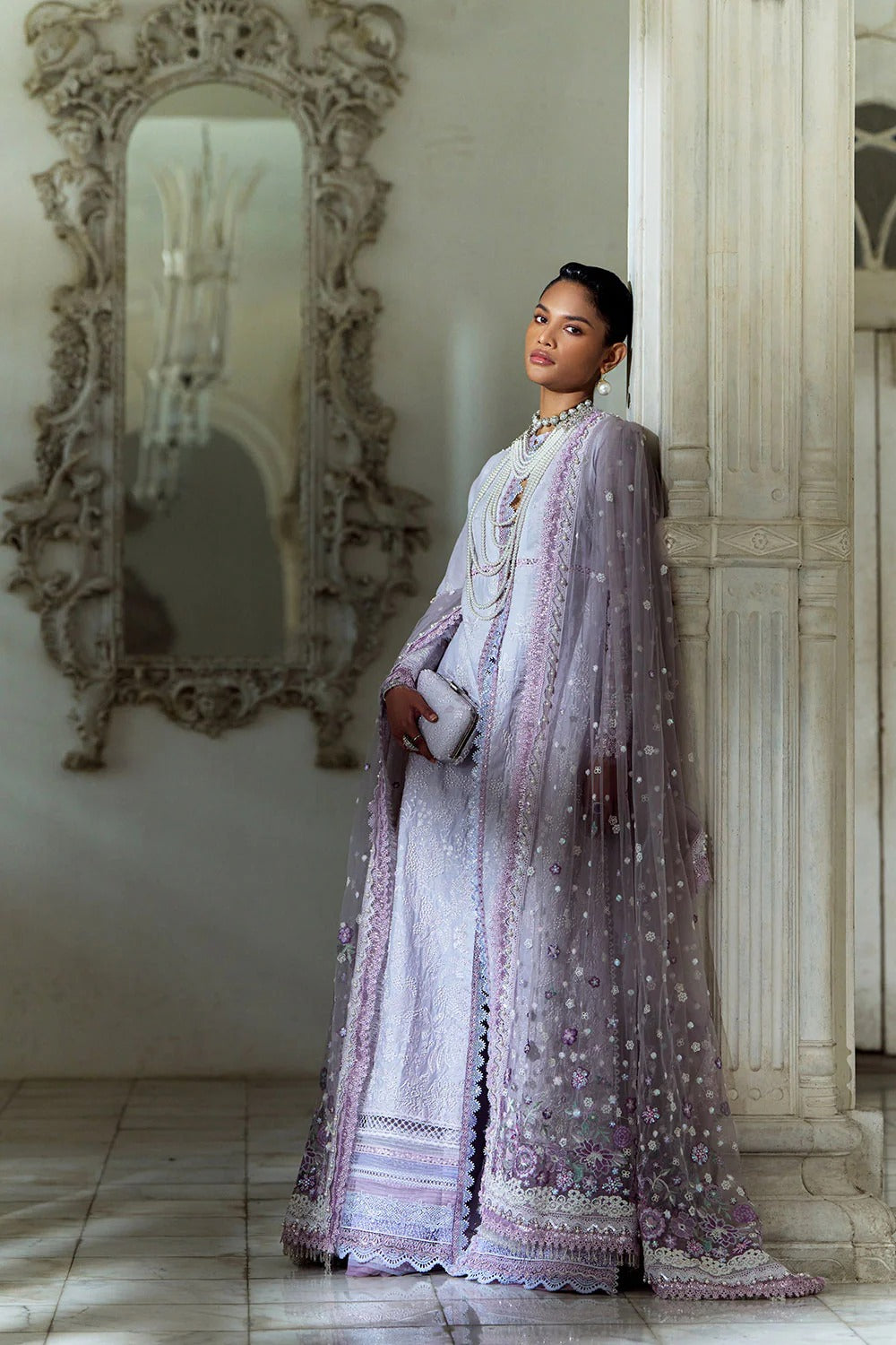 Woman in an elegant purple dress standing in a room with ornate mirror.