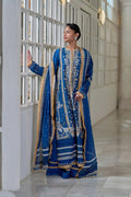 Woman in a blue embroidered traditional outfit standing in a modern indoor setting.