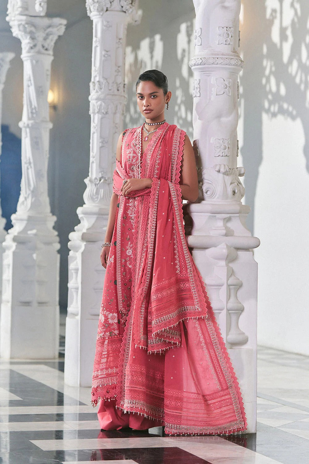 Woman in a pink traditional outfit standing against white marble columns.