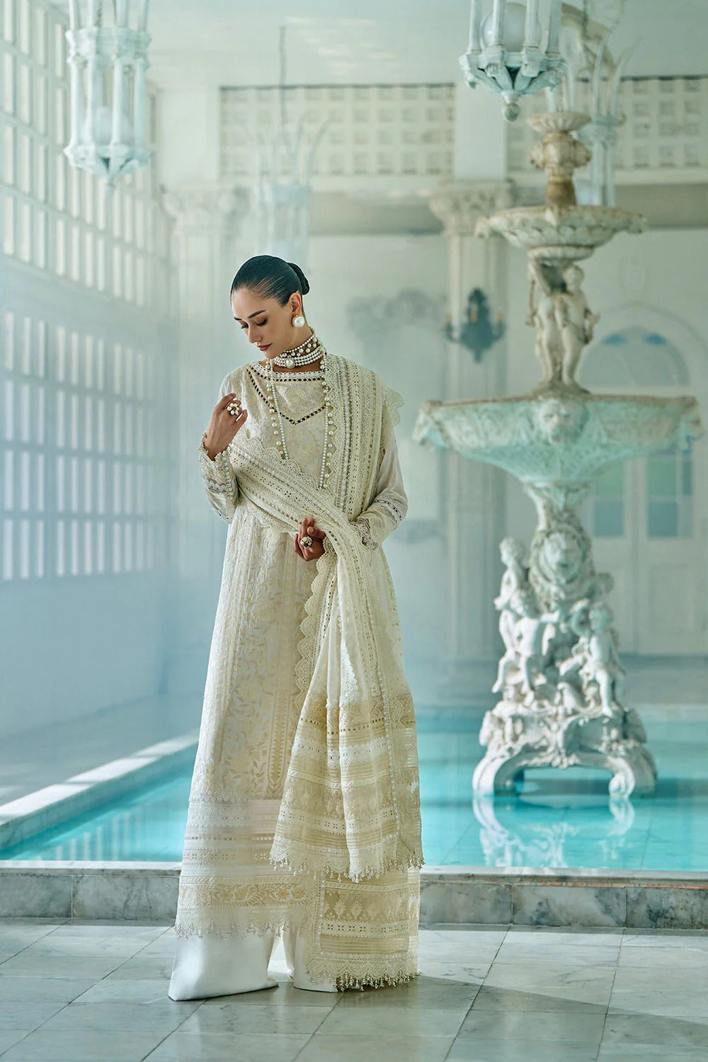 Woman in a traditional outfit standing in a luxurious room with a fountain and pool.