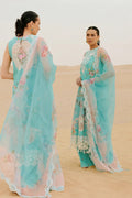 Woman in a light blue saree with floral patterns standing in a desert setting.