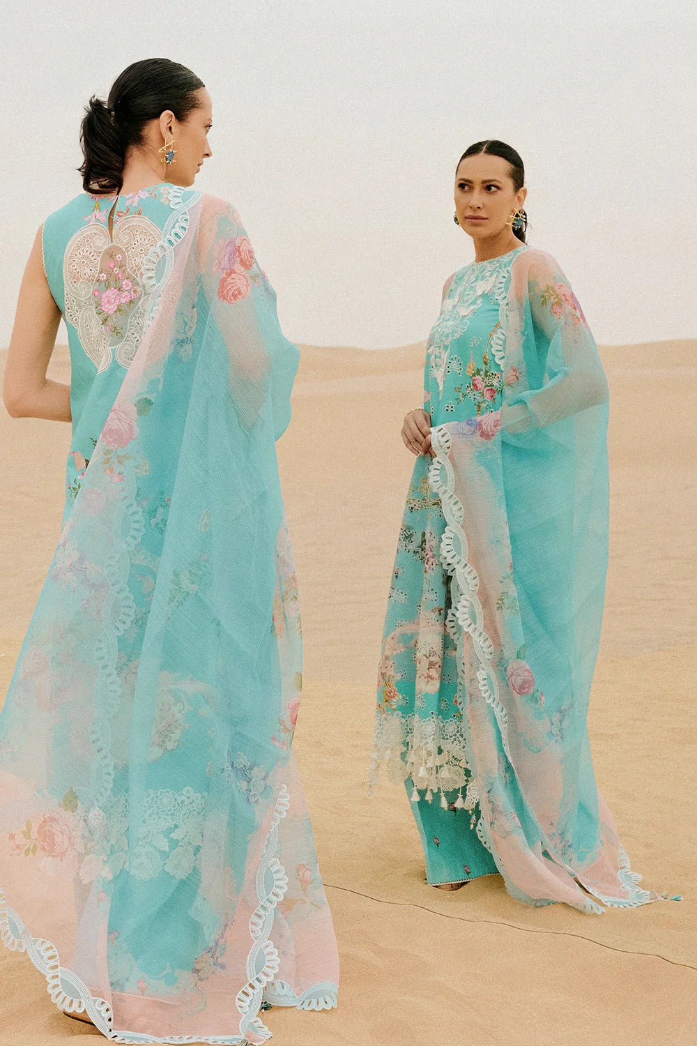 Woman in a light blue saree with floral patterns standing in a desert setting.