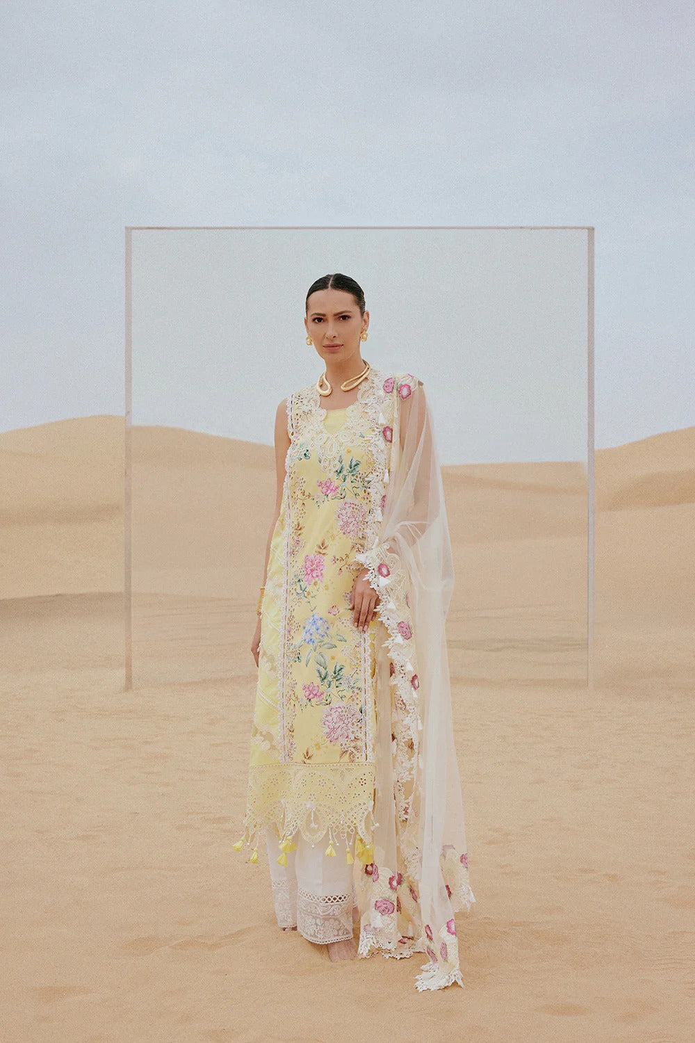 Woman in a floral dress standing in a desert landscape with a clear glass panel.