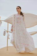 Woman in a white embroidered traditional outfit standing in a desert setting with a tent in the background.