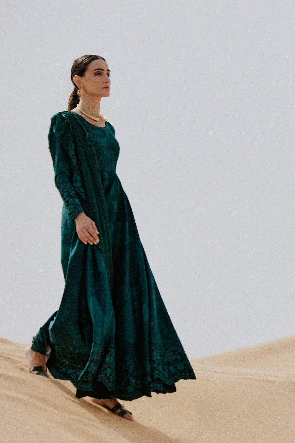 Woman in a dark green dress standing on sand dunes with a plain background