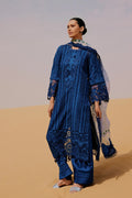 Woman in a blue embroidered outfit standing in a desert setting