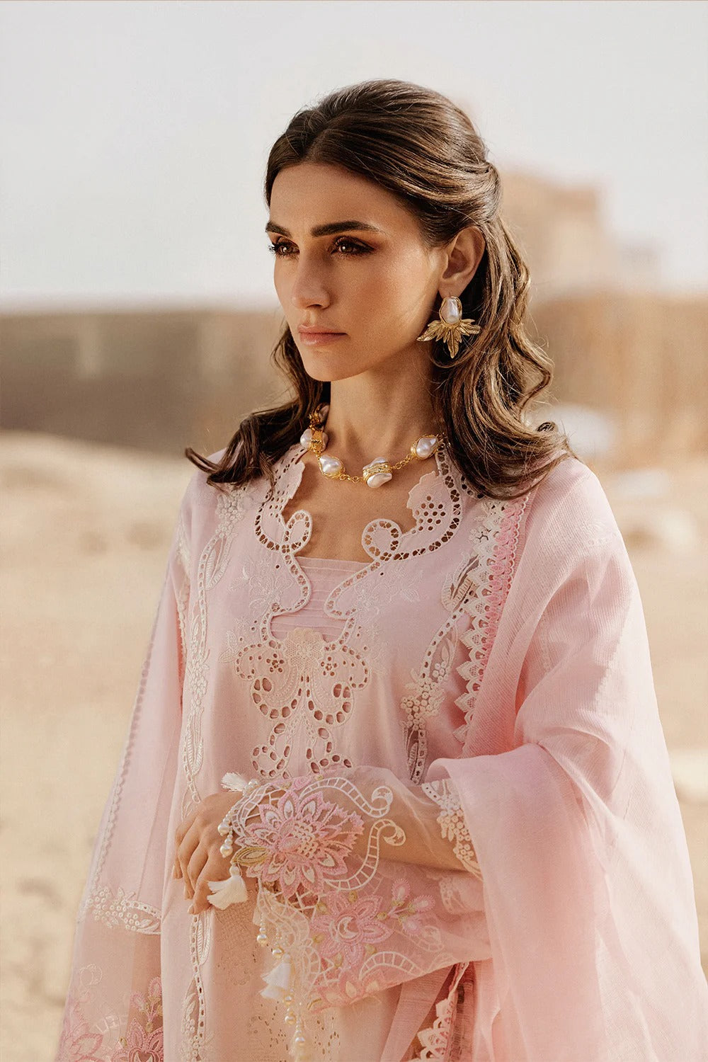 Woman in a pink embroidered outfit standing in a desert setting