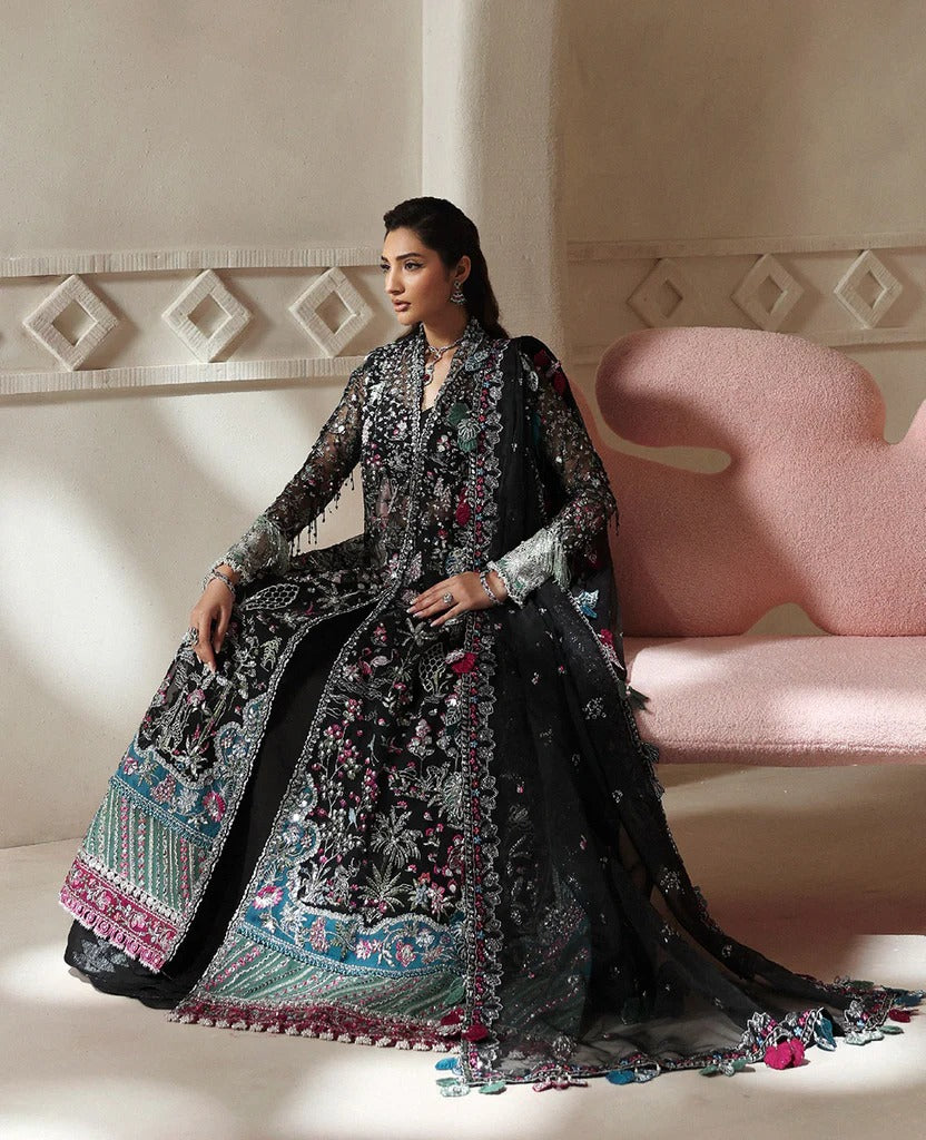 Woman in an elaborate black and multicolored traditional outfit sitting on a pink couch.