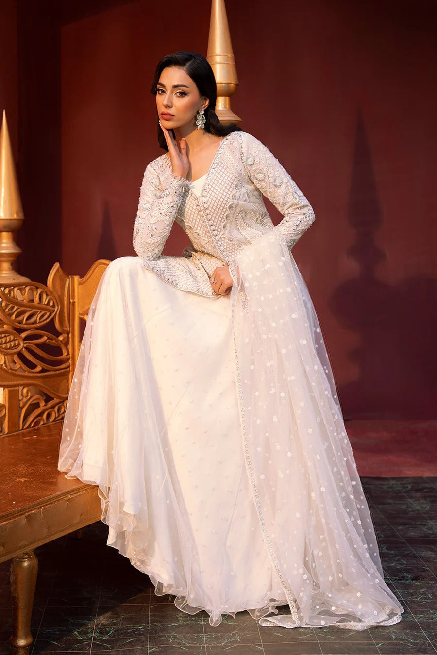 Woman in a white embroidered dress sitting on a wooden bench with a red background