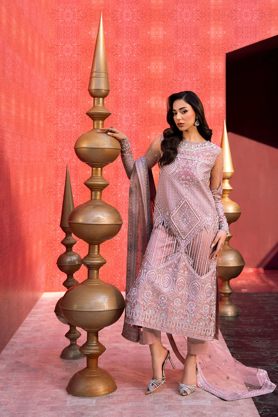 Woman in a pink traditional outfit standing next to decorative gold pillars against a red background