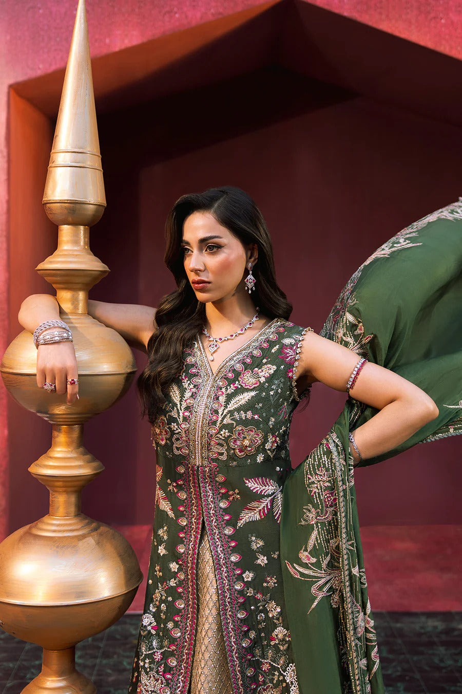 Woman in traditional embroidered outfit standing next to a decorative gold lamp.