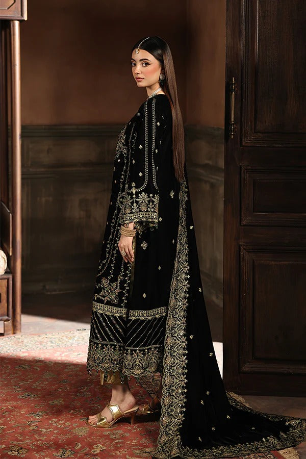 Woman in a black embroidered traditional outfit standing in a room with wooden paneling.