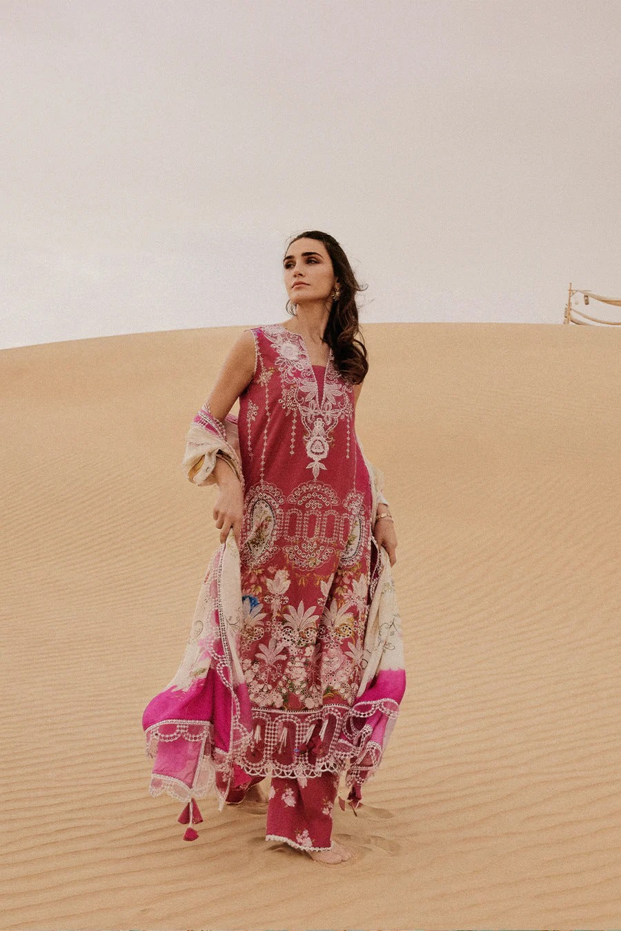 Woman in a pink and white embroidered dress standing on sand dunes