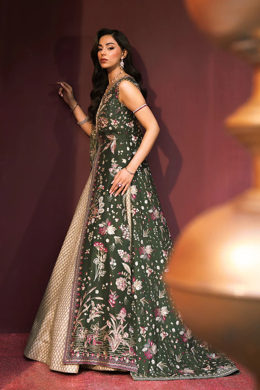 Woman in a dark green embroidered traditional outfit with gold details on a red background