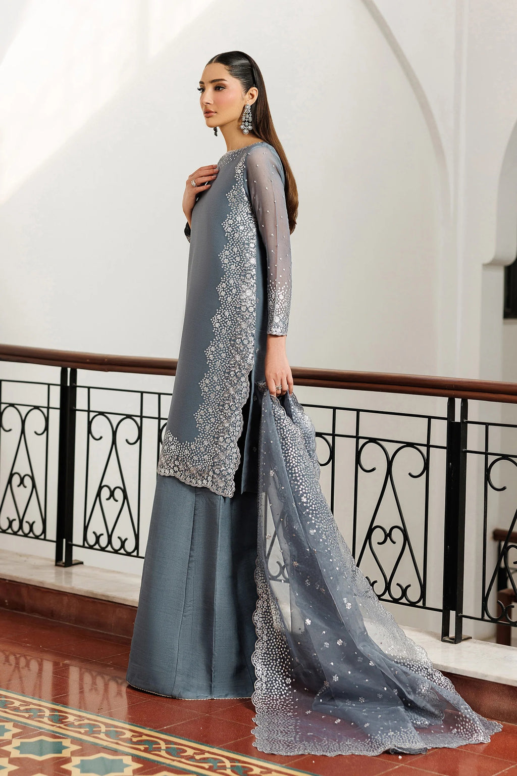 Woman in a gray traditional outfit with a matching dupatta in an elegant interior setting.