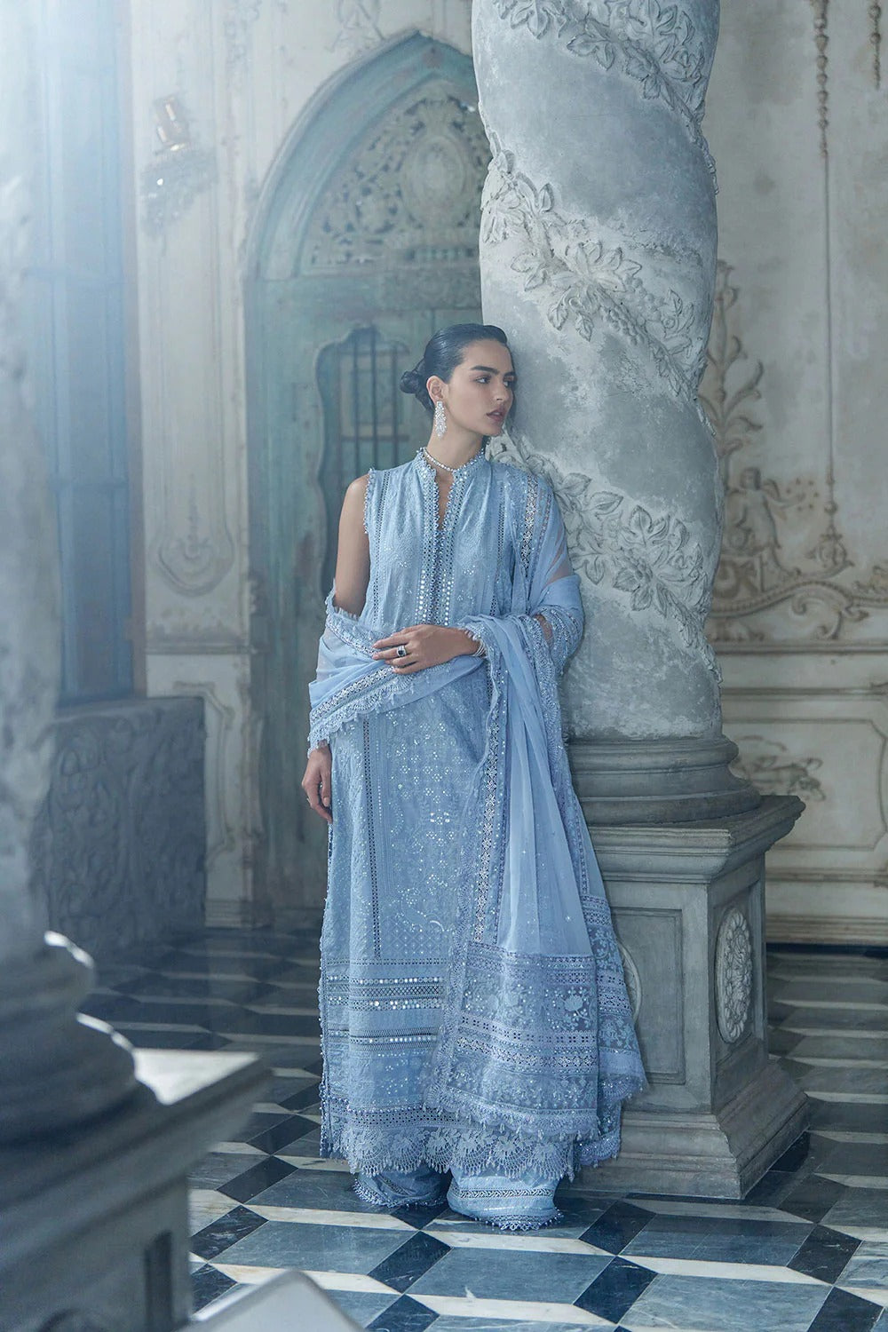 Woman in a light blue traditional outfit standing in an ornate architectural setting.