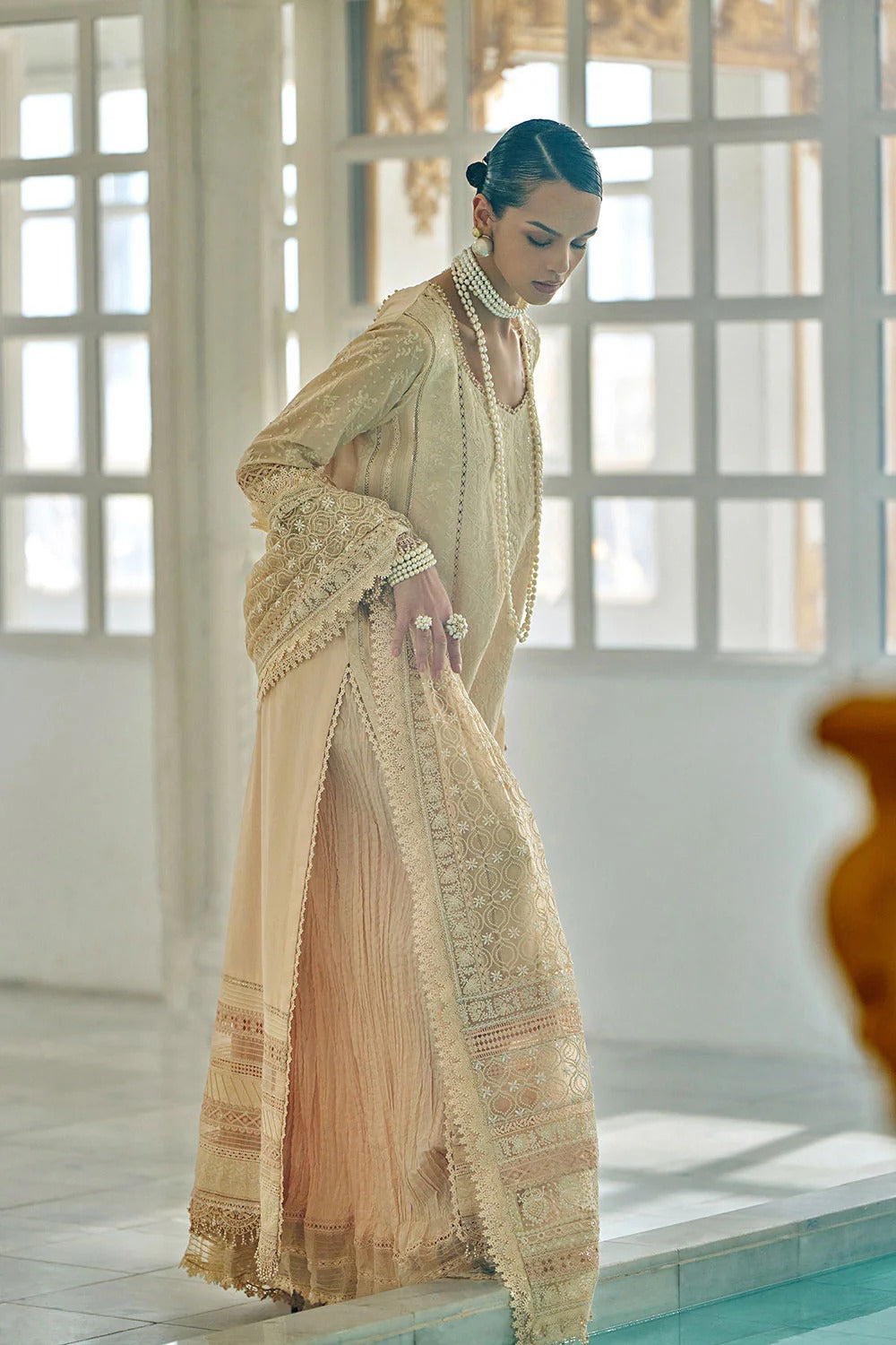 Woman in a traditional embroidered outfit standing by a pool with a neutral background