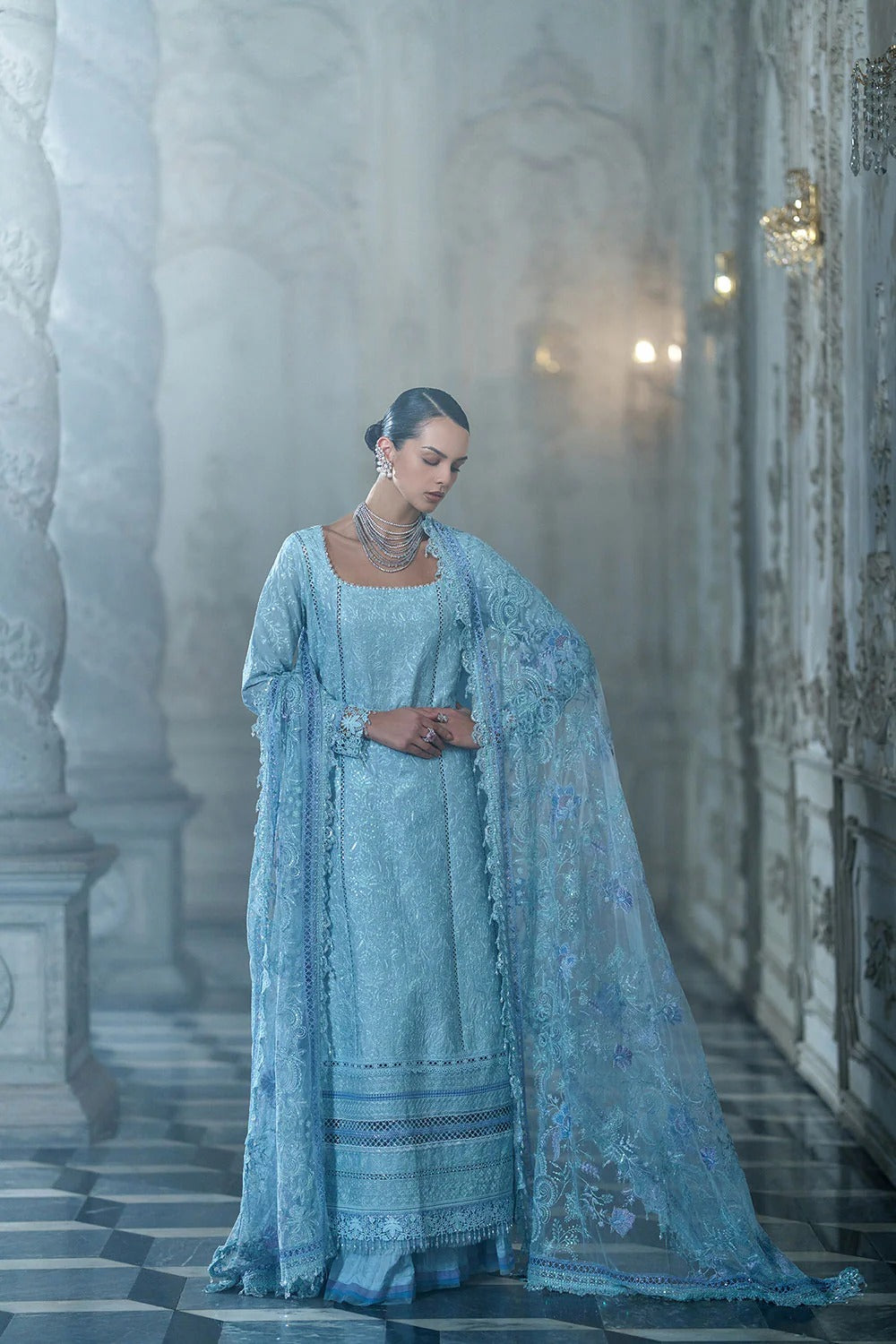 Woman in a light blue traditional outfit standing in an ornate hallway.