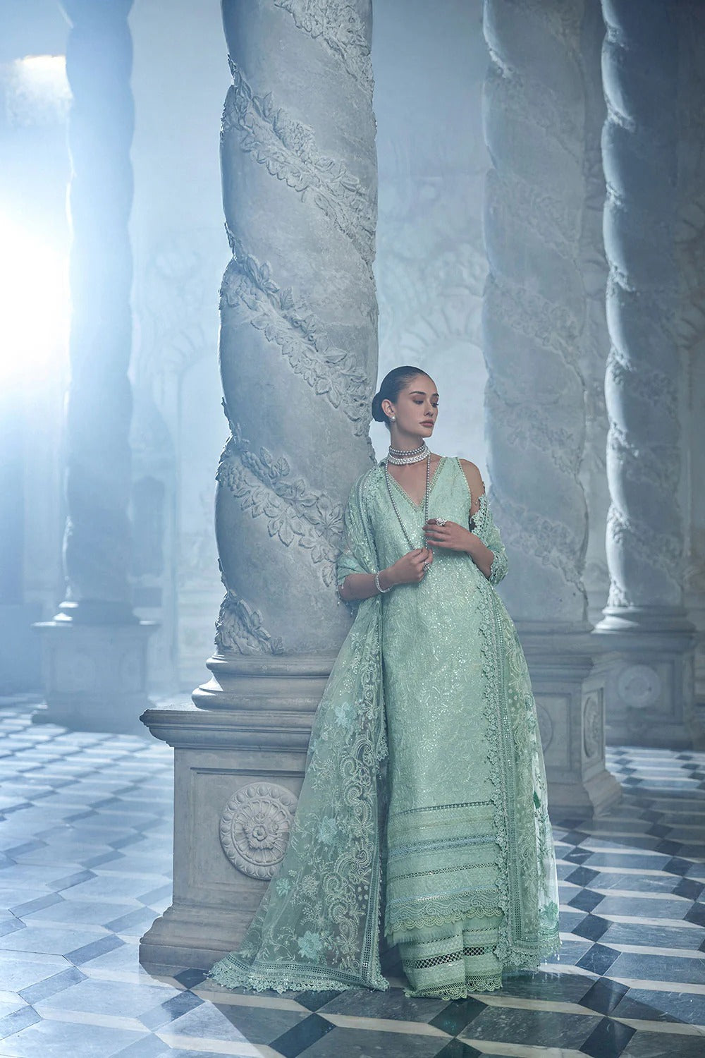 Woman in a light green dress standing in a grand, architecturally detailed room with columns.
