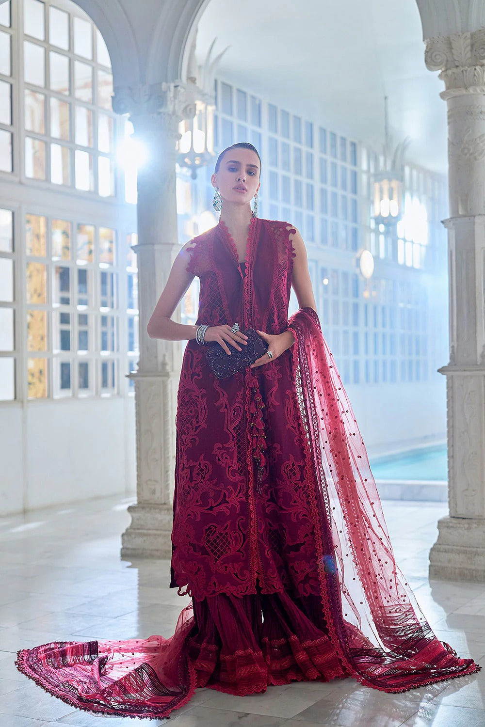 Woman in a red lace outfit standing in an elegant indoor setting with large windows.