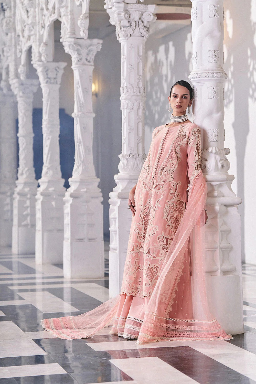 Woman in a pink traditional outfit standing in an elegant interior setting with white columns.