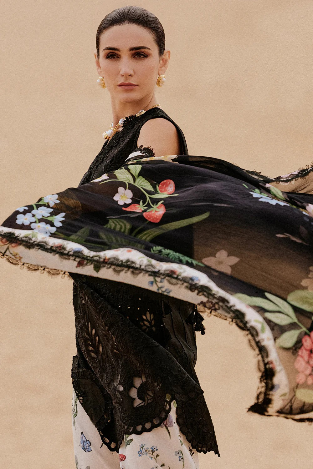 Woman holding a black embroidered shawl with floral patterns against a beige background