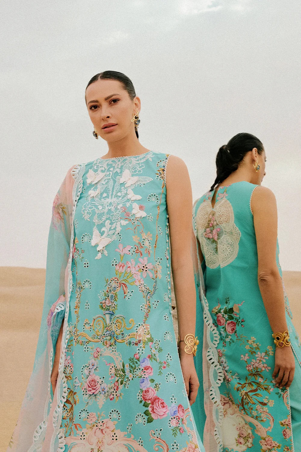 Woman wearing a turquoise embroidered dress with floral patterns in a desert setting.