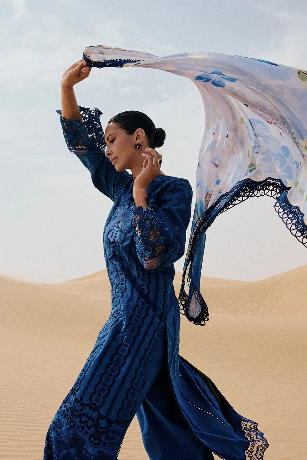 Woman in a blue embroidered outfit with a flowing fabric in a desert setting