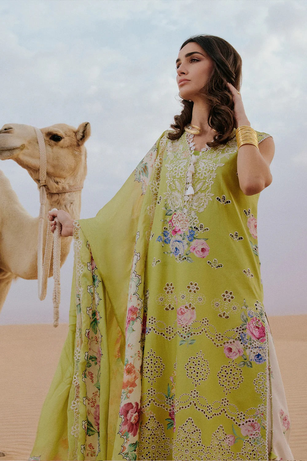 Woman in a yellow floral dress standing next to a camel in a desert setting