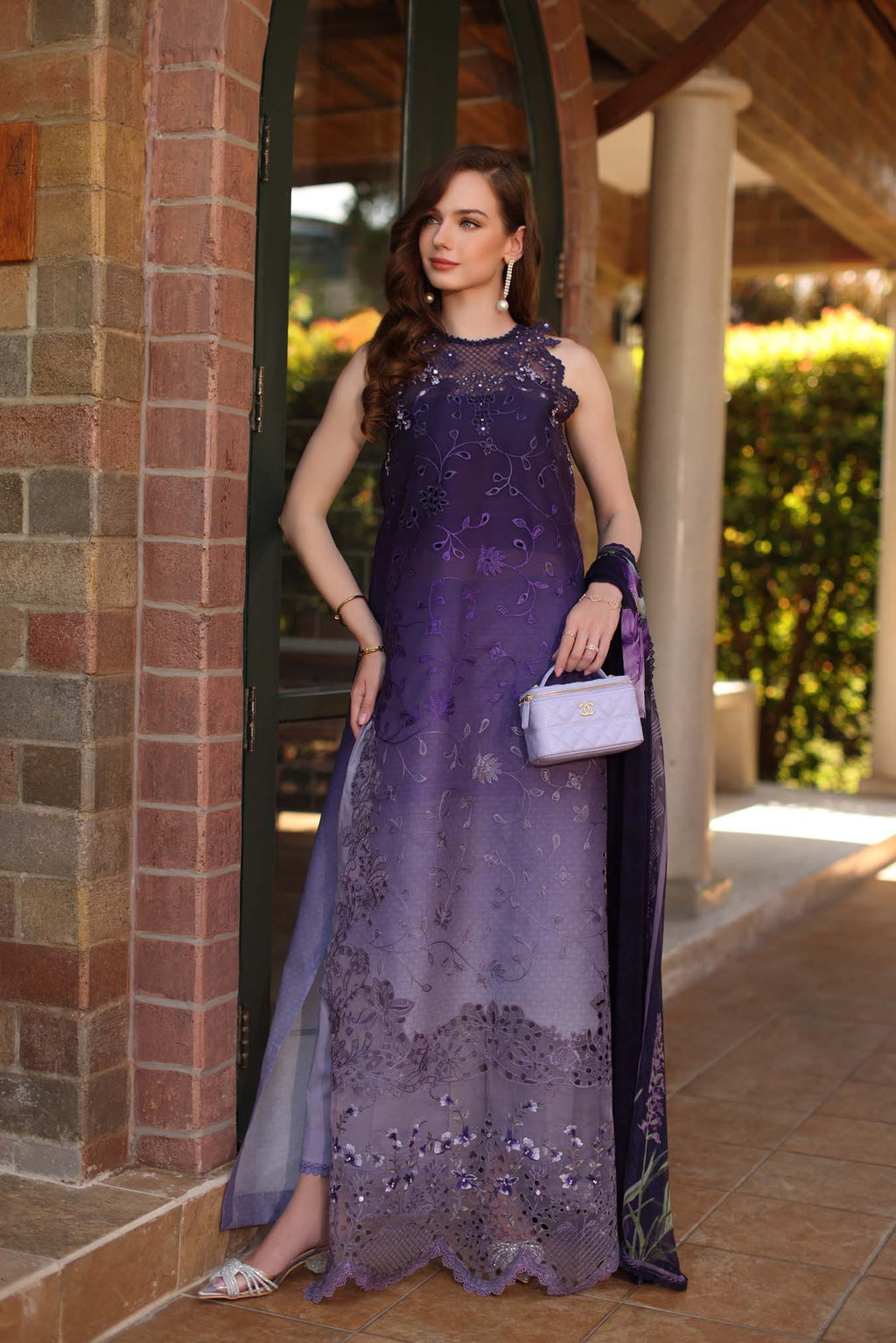 Woman in a purple lace dress standing outdoors near a building entrance.