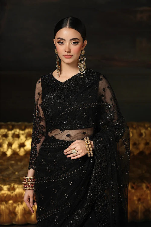 Woman wearing a black saree with gold jewelry against a dark background