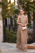 Woman in a beige embroidered dress standing outdoors with greenery in the background