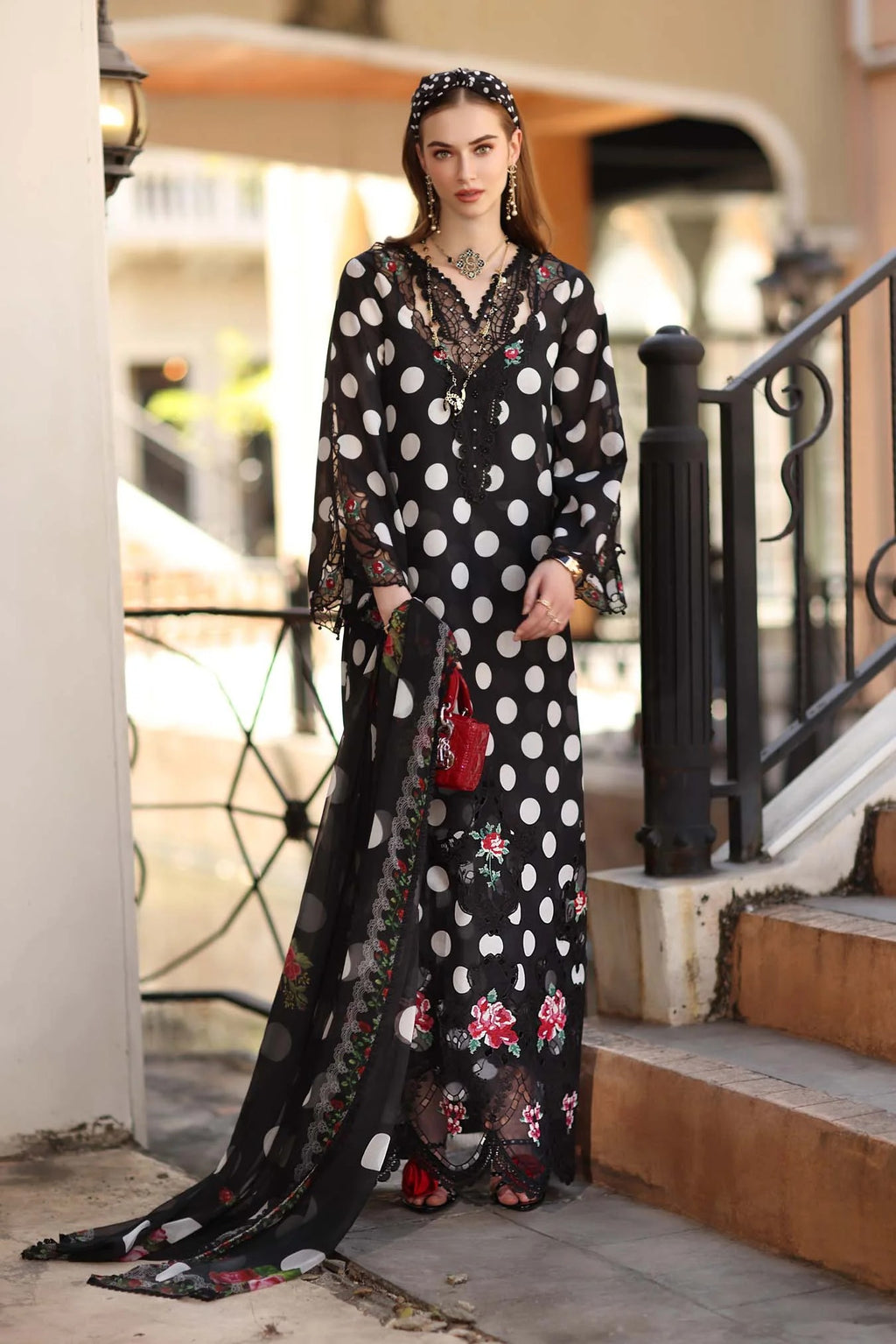Woman in a long, black and white polka dot dress with floral accents standing on steps.