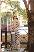 Woman in a polka dot dress with floral details standing outdoors near a tree.