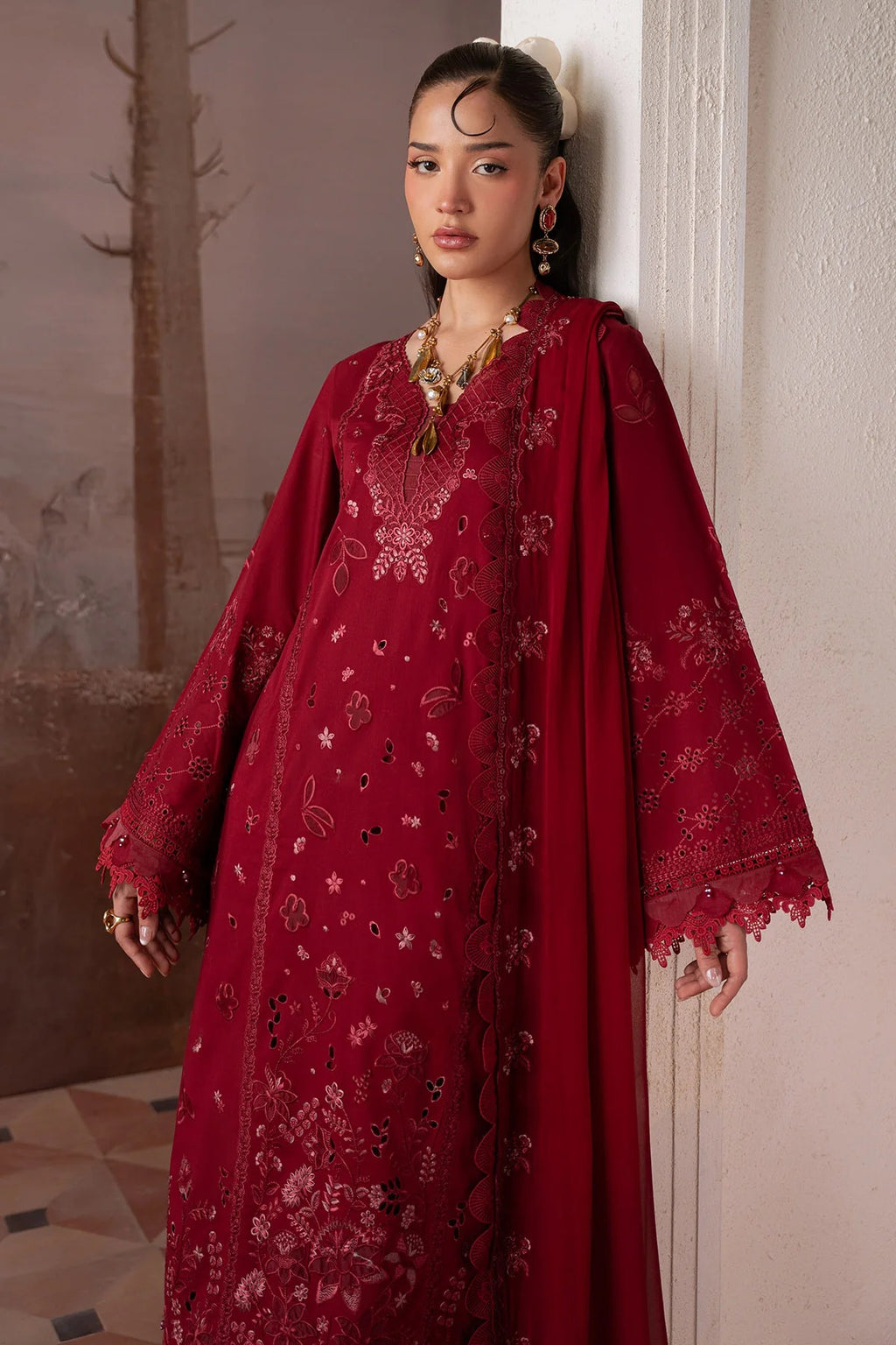 Woman wearing a red embroidered traditional outfit with a matching shawl indoors.