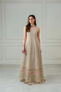 Woman wearing a long beige dress with floral patterns against a white paneled wall.