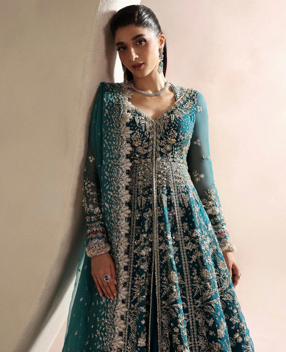 Woman wearing a teal and white embroidered traditional outfit against a plain background