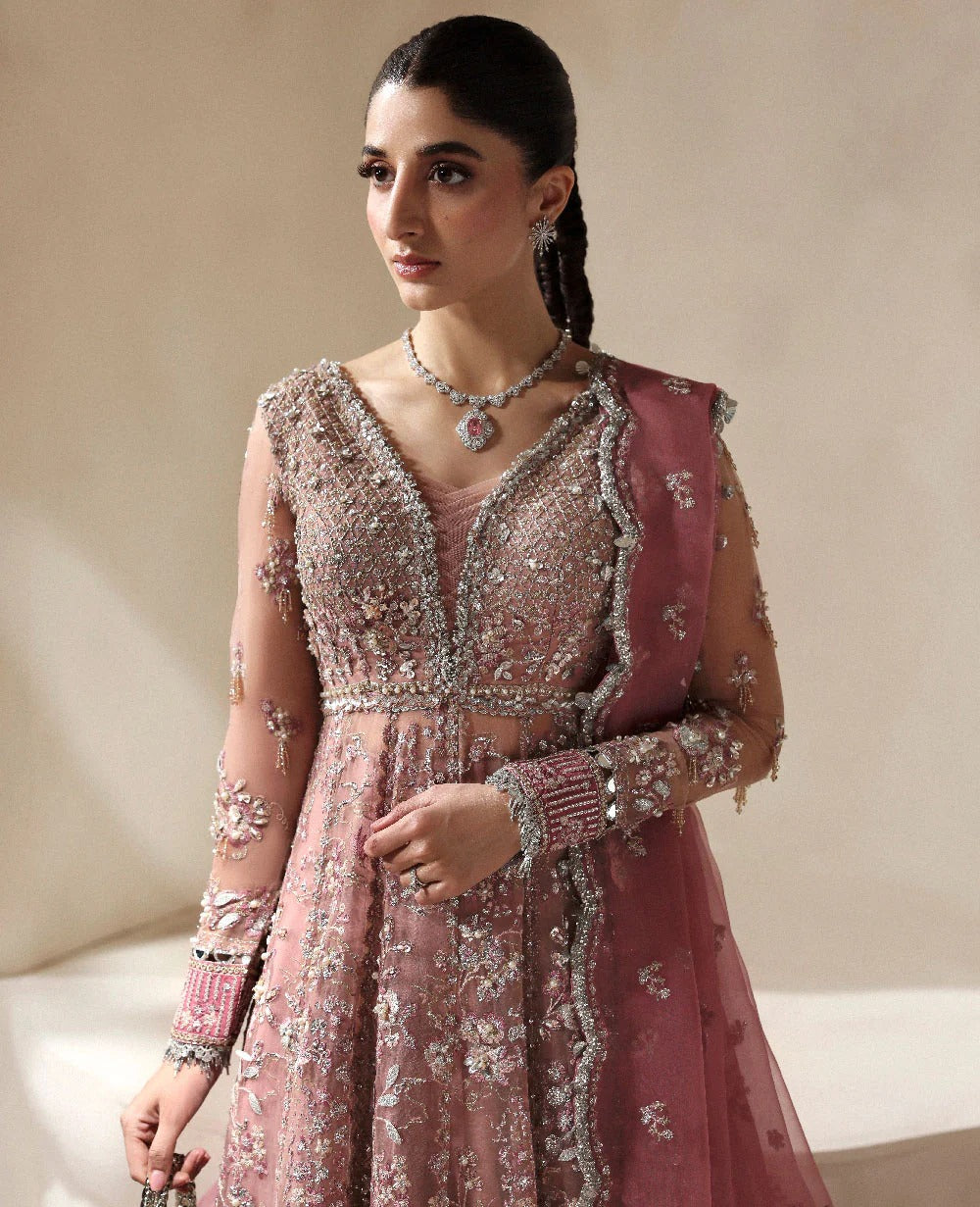 Woman wearing a pink embroidered traditional outfit with a necklace against a neutral background