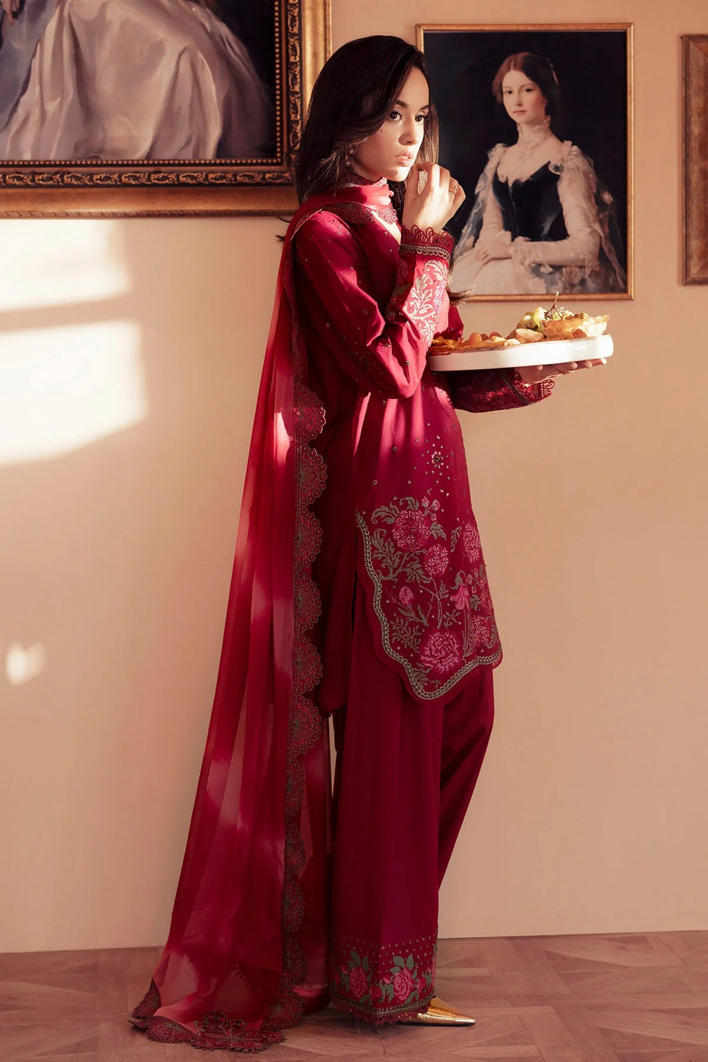 Woman in a red embroidered outfit holding a tray with food in an elegant room.
