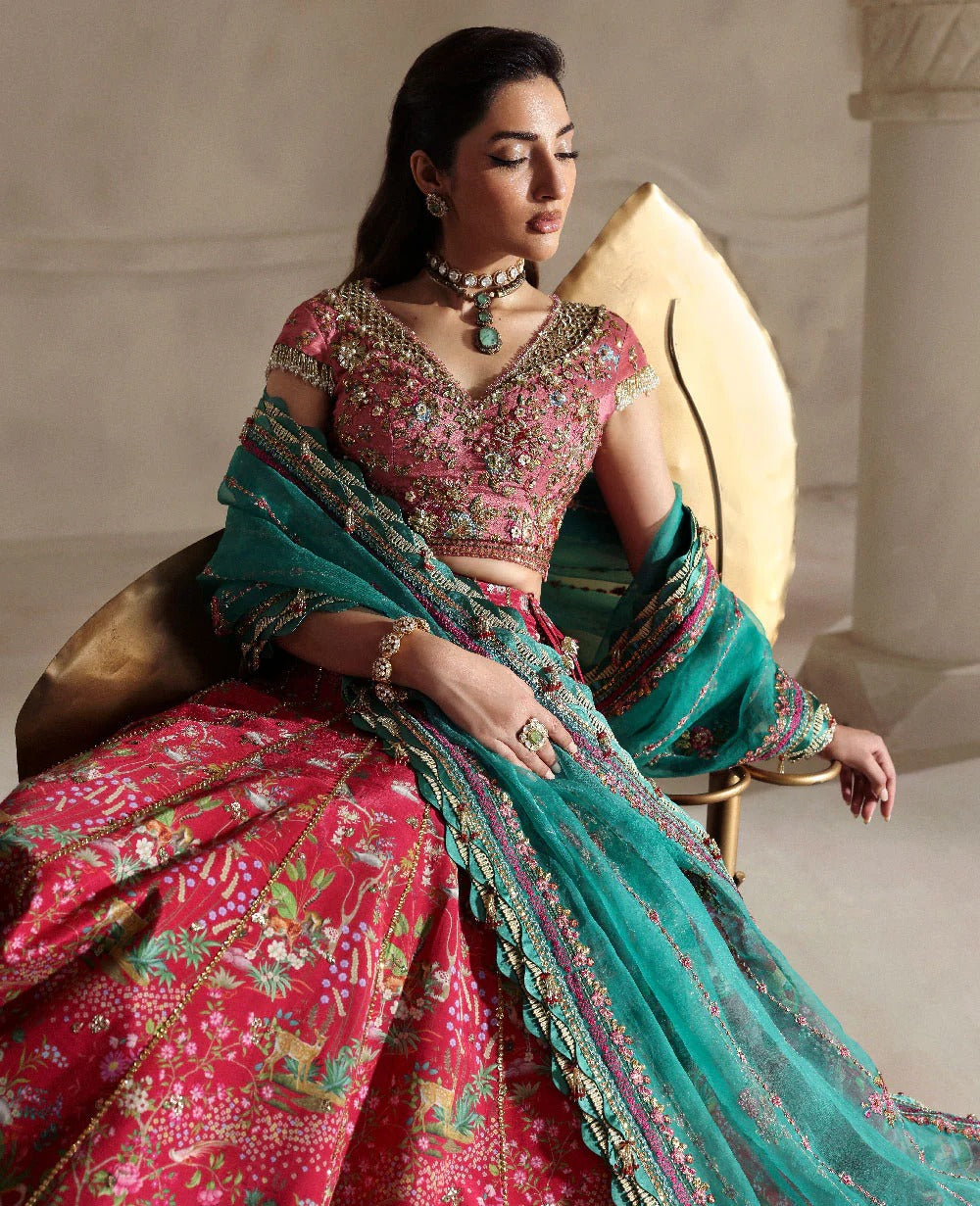 Woman in a traditional pink and green saree sitting on a decorative chair.