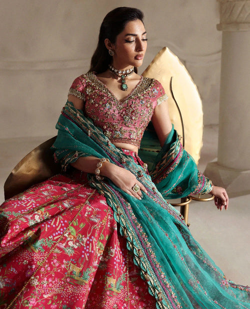 Woman in a traditional pink and green saree sitting on a decorative chair.