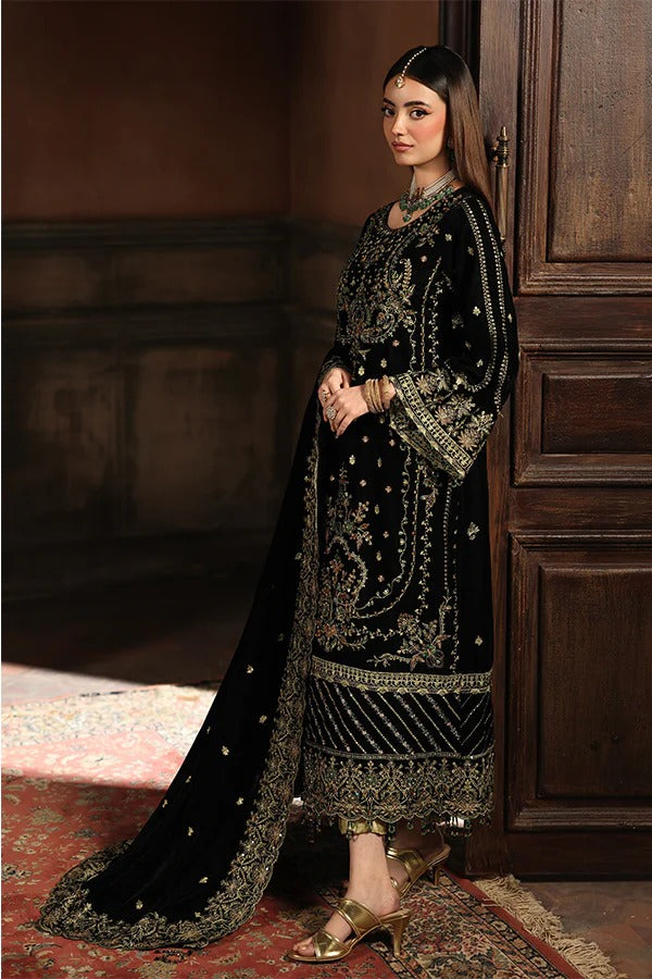 Woman in a black embroidered traditional outfit standing in a dimly lit room.