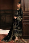 Woman in a black embroidered traditional outfit standing in a dimly lit room.