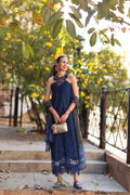 Woman in a blue dress standing outdoors with greenery and a fence in the background